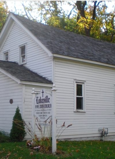Historic white wood-frame meeting house in Nassau County surrounded by trees, representing early religious life on Long Island.