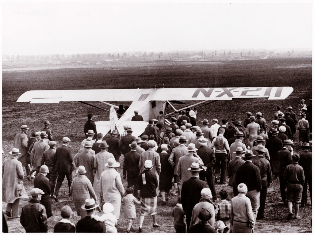 Historic crowd gathered around an early airplane at an airfield in Nassau County, Long Island, reflecting the region’s aviation history.