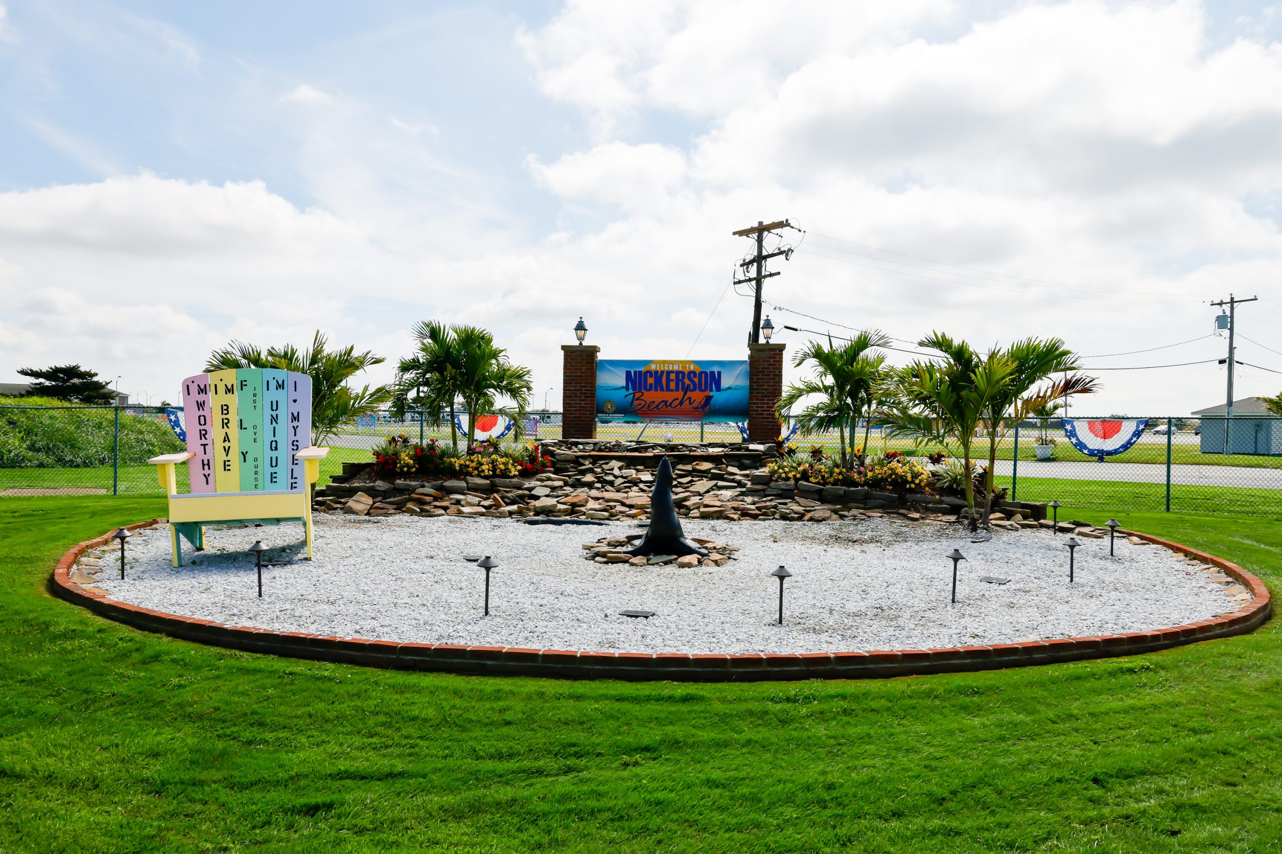 Colorful entrance display at Nickerson Beach Park in Lido Beach, Nassau County, featuring tropical landscaping, a beach sign, and a decorative Adirondack chair.