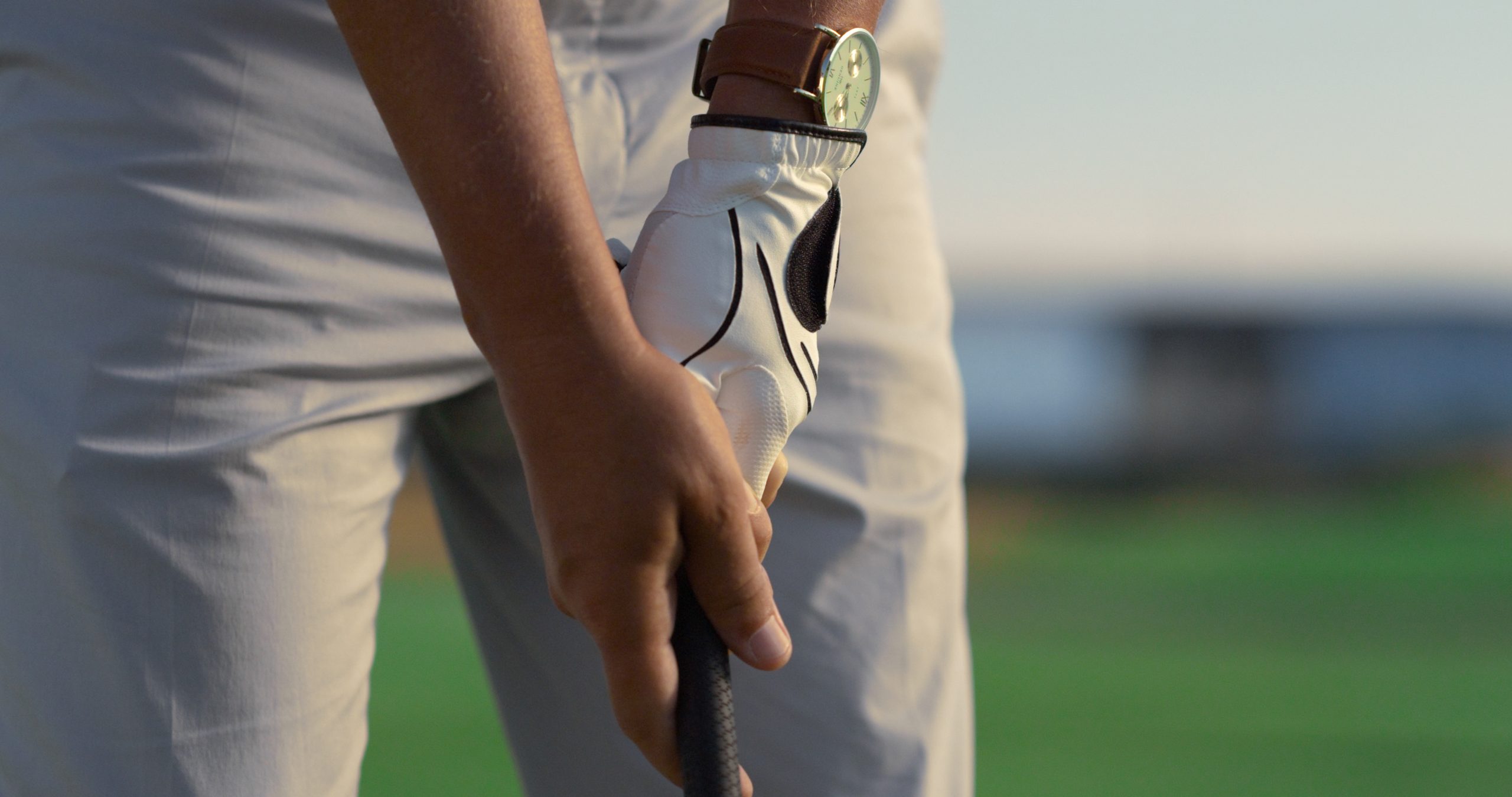 Close-up of a golfer gripping a golf club while preparing for a shot on a sunny day.