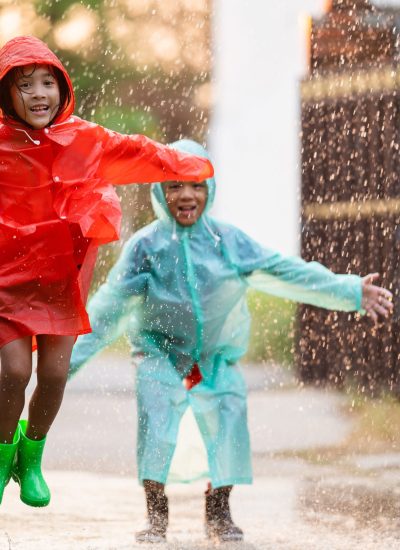 Children wearing raincoats and boots playing outside in the rain.