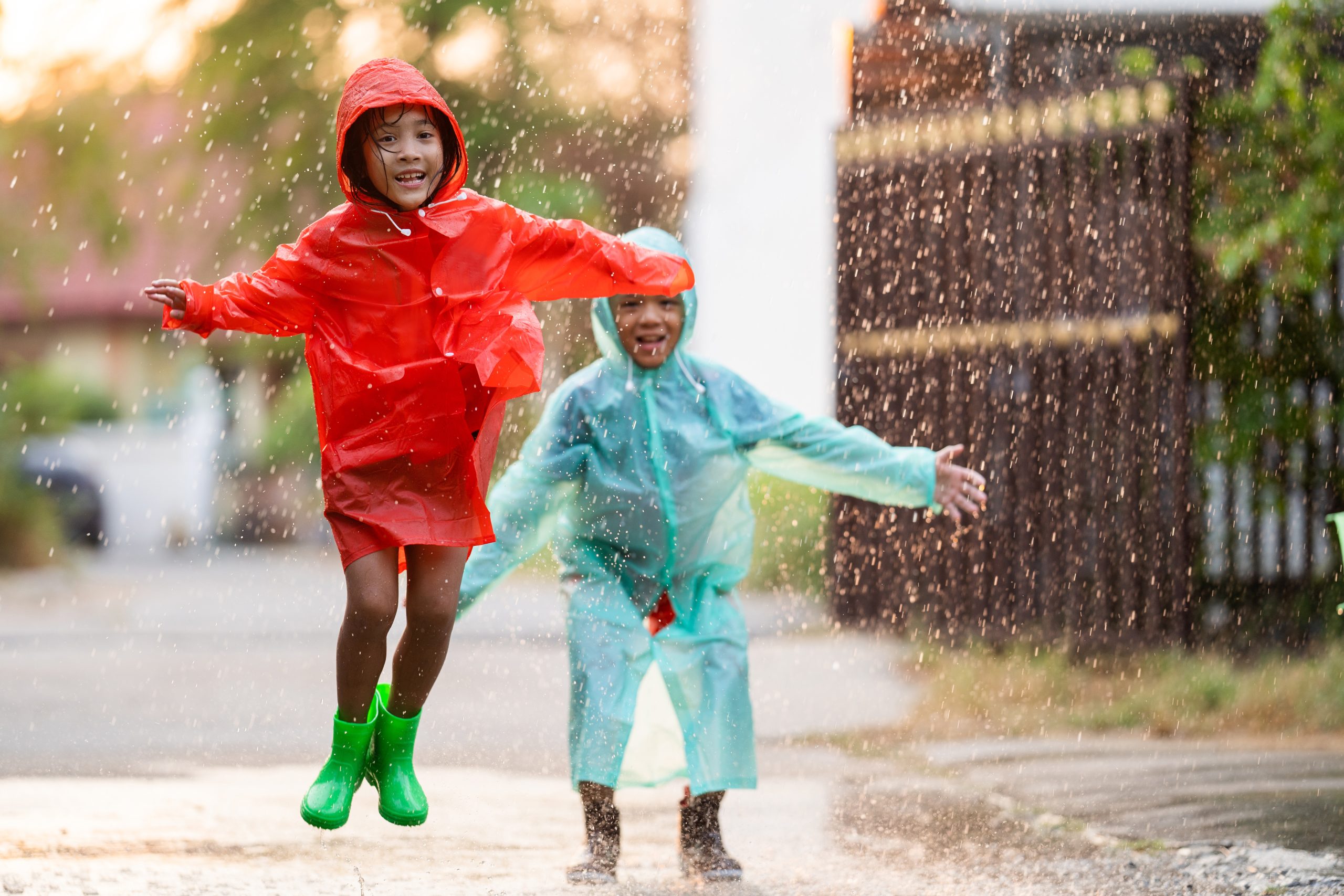 Children wearing raincoats and boots playing outside in the rain.